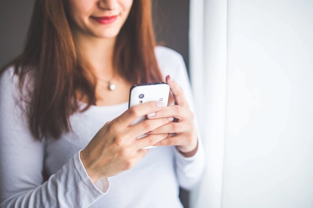 A woman is holding her phone in front of the window.